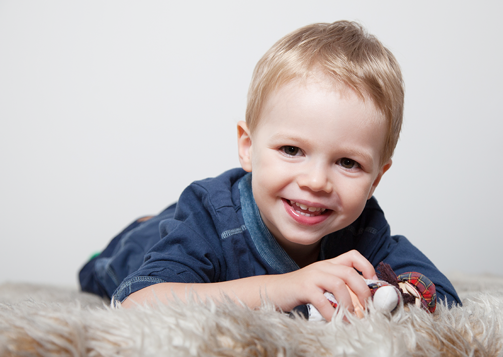 kleiner Junge auf dem Bauch liegend und mit erhobenen Kopf lachend - Familienfotos, Kinderfotos, Familienfotografie, Kinderfotografie, Familienbilder